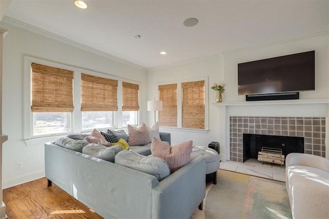 living room with a tiled fireplace, ornamental molding, and light wood-type flooring