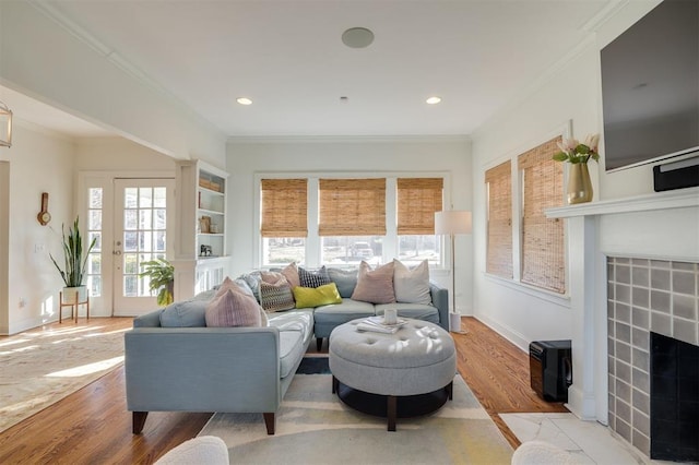 living room featuring a tiled fireplace, ornamental molding, and light hardwood / wood-style flooring