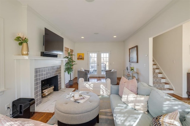 living room with a tiled fireplace, ornamental molding, light hardwood / wood-style flooring, and french doors