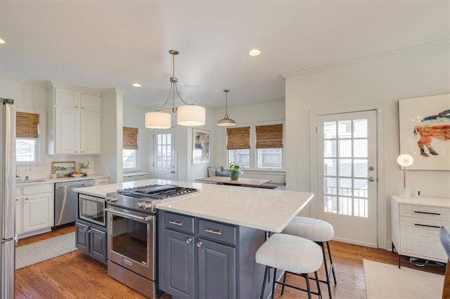 kitchen featuring stainless steel appliances, a kitchen island, pendant lighting, and white cabinets