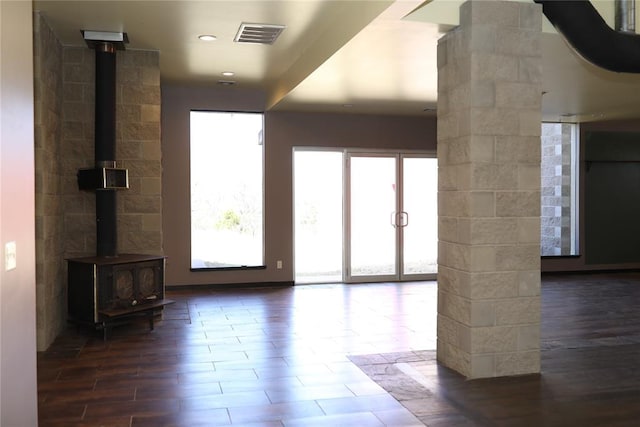 unfurnished living room with visible vents, dark wood-type flooring, and a wood stove