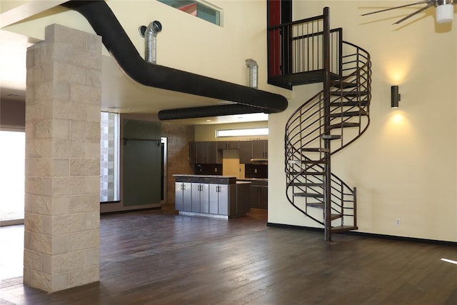 unfurnished living room featuring a ceiling fan, dark wood-style flooring, and a towering ceiling