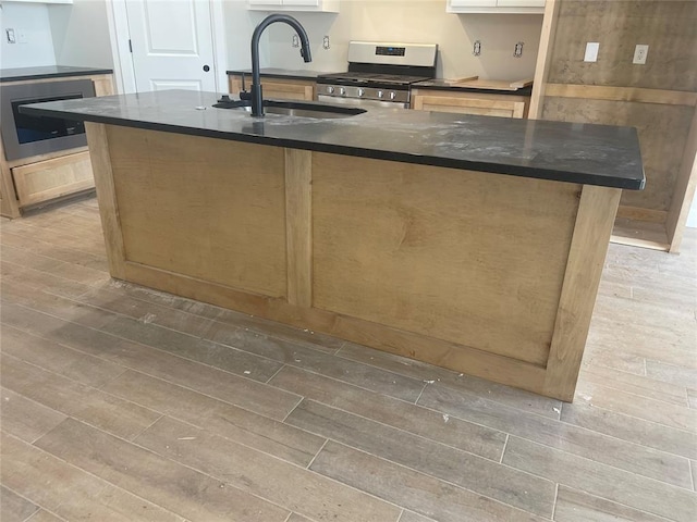 kitchen with wood-type flooring, appliances with stainless steel finishes, sink, and a center island with sink