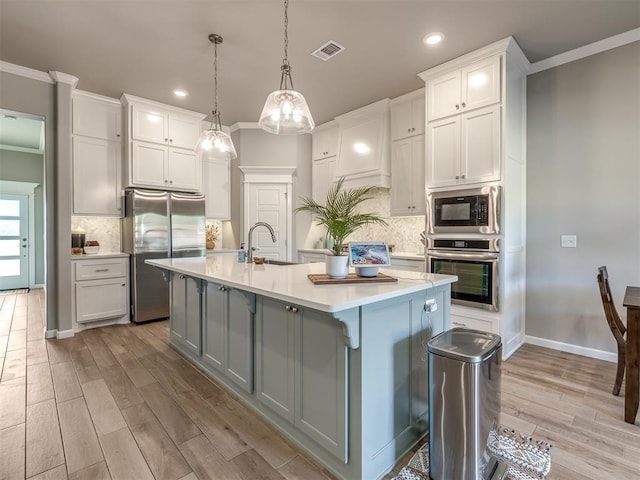 kitchen featuring appliances with stainless steel finishes, pendant lighting, white cabinetry, a kitchen island with sink, and light wood-type flooring