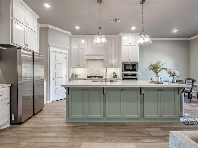 kitchen with white cabinetry, appliances with stainless steel finishes, a kitchen island with sink, and decorative light fixtures