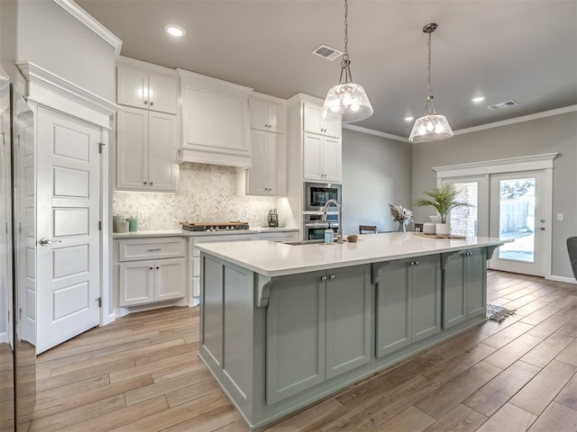 kitchen with decorative light fixtures, appliances with stainless steel finishes, white cabinets, and a center island with sink