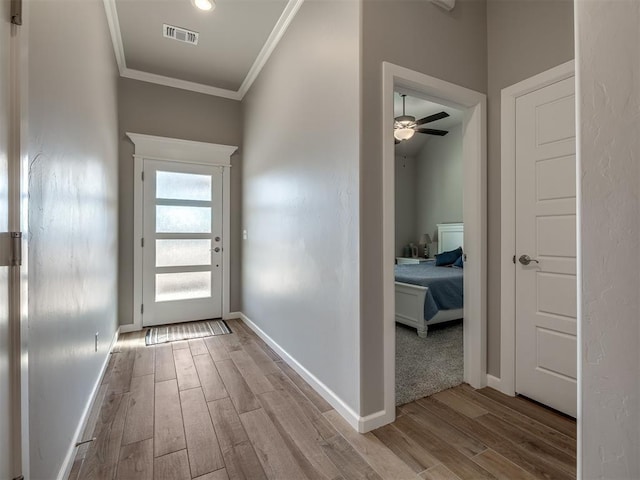 doorway with ornamental molding, ceiling fan, and light wood-type flooring