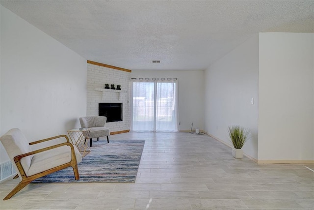 living room featuring a brick fireplace, a textured ceiling, and light wood-type flooring