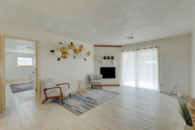 living room with a brick fireplace, light hardwood / wood-style floors, and a textured ceiling