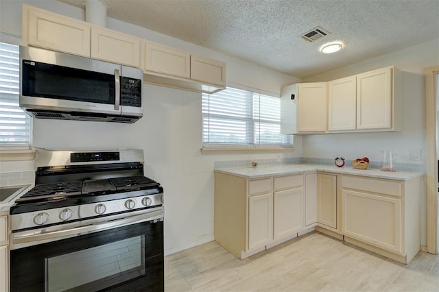 kitchen with light hardwood / wood-style floors, a textured ceiling, and appliances with stainless steel finishes