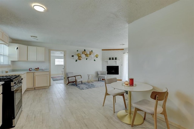 dining room with a brick fireplace, plenty of natural light, a textured ceiling, and light wood-type flooring