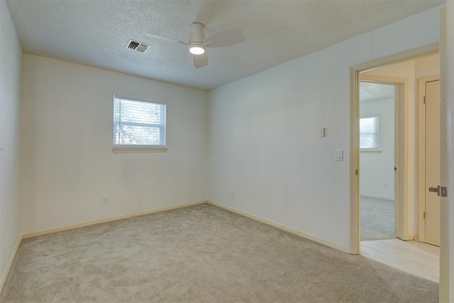 empty room featuring ceiling fan, a healthy amount of sunlight, light carpet, and a textured ceiling