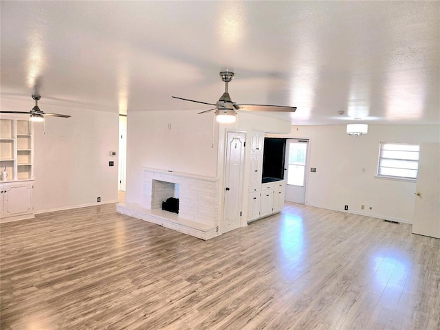 unfurnished living room with ceiling fan, a brick fireplace, and light wood-type flooring