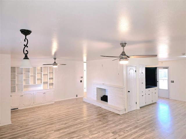 unfurnished living room with ceiling fan, a brick fireplace, built in features, and light wood-type flooring