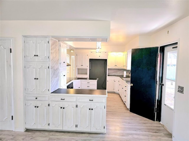 kitchen with light hardwood / wood-style flooring, white cabinetry, black fridge, decorative backsplash, and kitchen peninsula