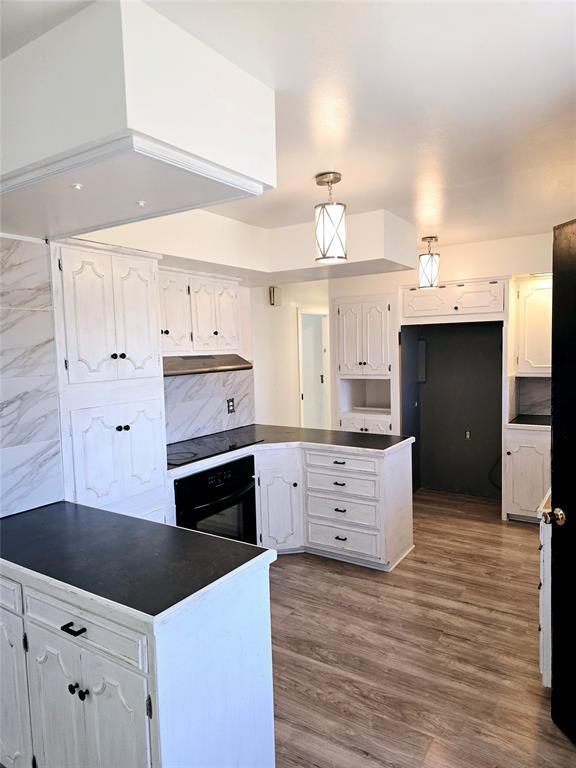 kitchen featuring wood-type flooring, hanging light fixtures, black oven, decorative backsplash, and white cabinets