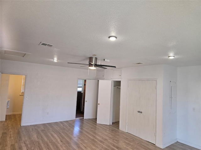 unfurnished bedroom with ceiling fan, light wood-type flooring, electric panel, and a textured ceiling