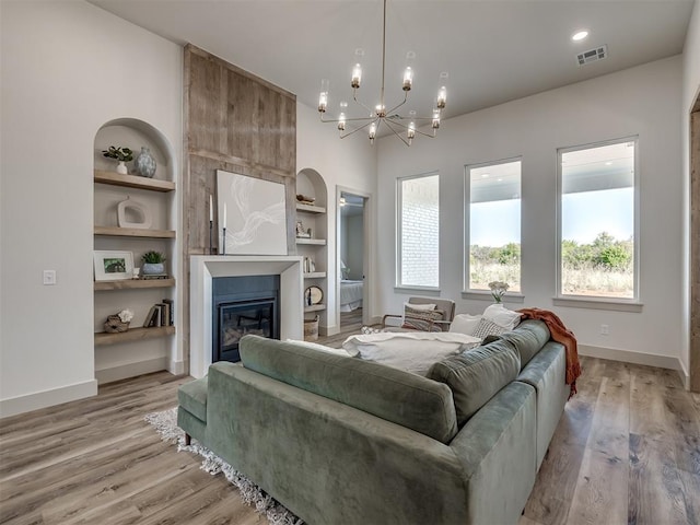 living room with a large fireplace, built in features, a chandelier, and light hardwood / wood-style flooring