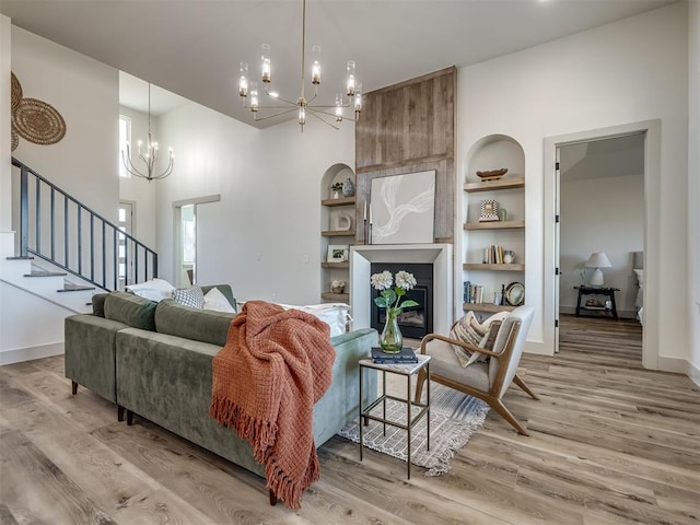 living room featuring a fireplace, light wood-type flooring, built in features, and a notable chandelier