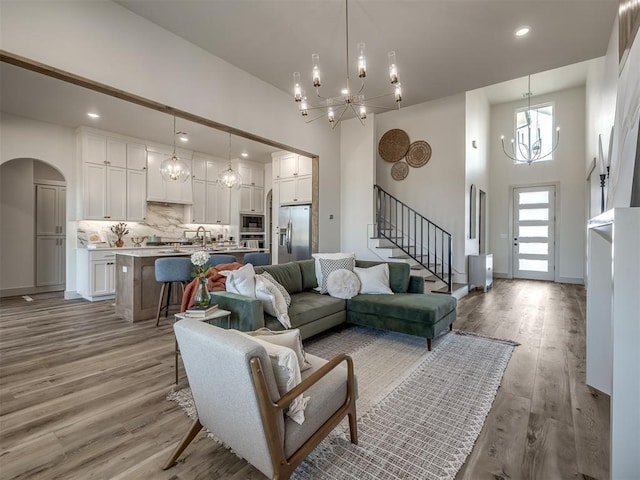 living room featuring a towering ceiling, a chandelier, sink, and light wood-type flooring