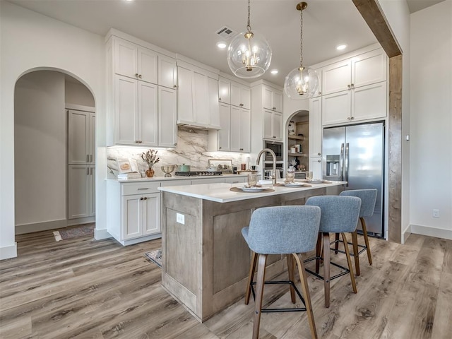 kitchen with appliances with stainless steel finishes, pendant lighting, white cabinetry, an island with sink, and light wood-type flooring