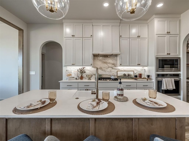 kitchen with white cabinetry, decorative backsplash, a kitchen island with sink, stainless steel appliances, and custom range hood