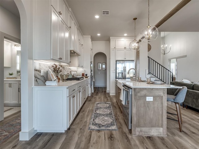 kitchen featuring white cabinetry, decorative light fixtures, a center island with sink, appliances with stainless steel finishes, and a kitchen breakfast bar