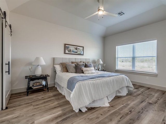 bedroom with lofted ceiling, ceiling fan, light hardwood / wood-style floors, a raised ceiling, and a barn door