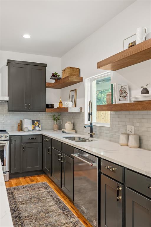 kitchen with sink, backsplash, light stone counters, stainless steel appliances, and light hardwood / wood-style flooring