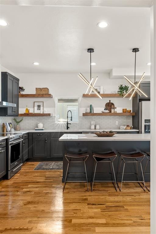 kitchen with high quality fridge, stainless steel stove, decorative light fixtures, and a kitchen bar