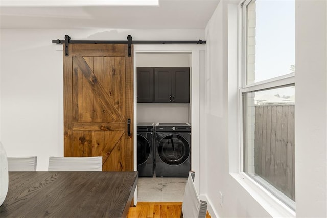 washroom featuring cabinets, washing machine and dryer, a barn door, and light hardwood / wood-style flooring