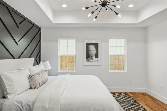 bedroom with a raised ceiling, hardwood / wood-style flooring, and multiple windows