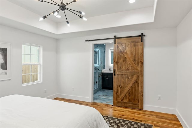 bedroom featuring ensuite bathroom, a barn door, hardwood / wood-style floors, and a tray ceiling