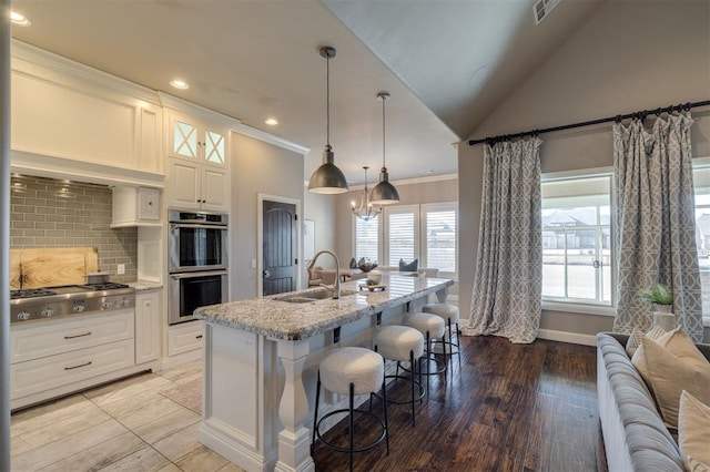 kitchen featuring sink, tasteful backsplash, white cabinetry, a center island with sink, and appliances with stainless steel finishes