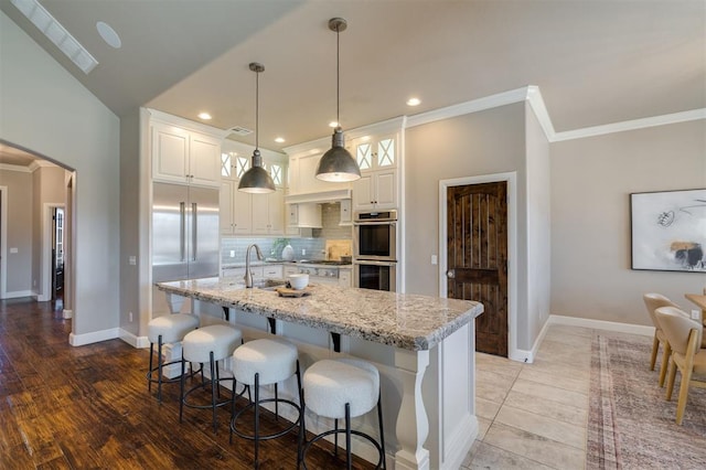 kitchen with white cabinetry, stainless steel appliances, light stone counters, an island with sink, and decorative light fixtures