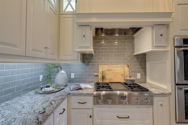 kitchen with stainless steel appliances, white cabinetry, light stone countertops, and backsplash