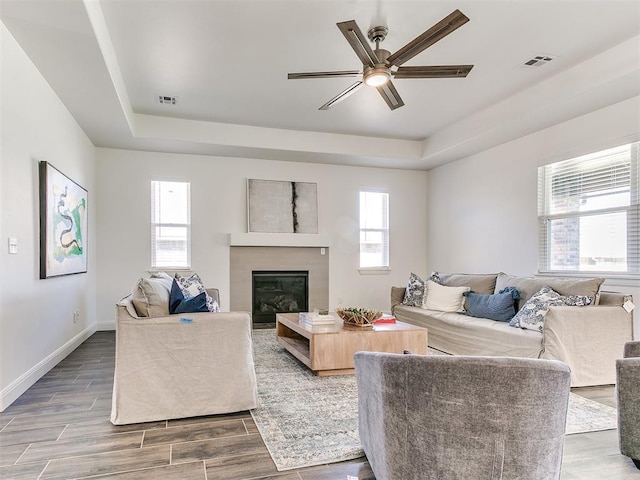 living room with a raised ceiling, plenty of natural light, and ceiling fan