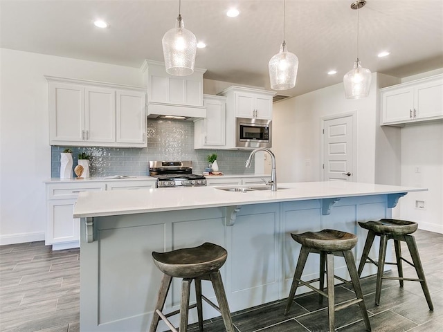 kitchen featuring pendant lighting, white cabinets, stainless steel appliances, and a large island with sink