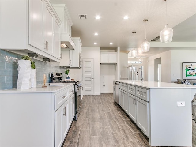 kitchen with sink, hanging light fixtures, appliances with stainless steel finishes, a kitchen island with sink, and white cabinets