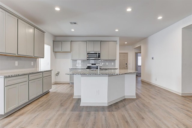 kitchen featuring light stone countertops, stainless steel appliances, gray cabinets, and a center island with sink