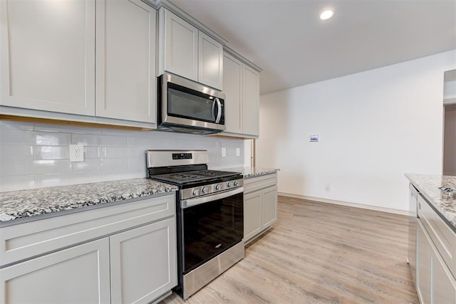 kitchen with light stone counters, appliances with stainless steel finishes, decorative backsplash, and light hardwood / wood-style flooring