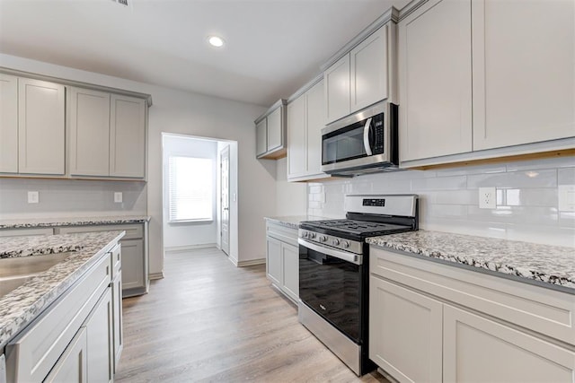 kitchen with appliances with stainless steel finishes, gray cabinetry, backsplash, light stone counters, and light hardwood / wood-style flooring