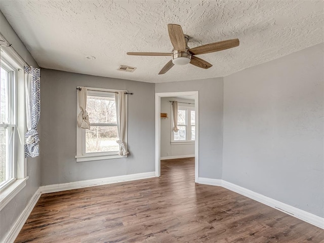 spare room featuring a wealth of natural light, visible vents, baseboards, and wood finished floors