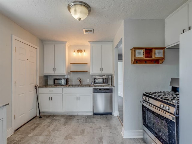 kitchen featuring stainless steel appliances, visible vents, decorative backsplash, white cabinets, and a sink