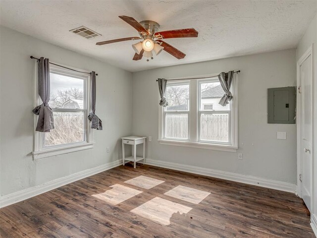 unfurnished room featuring a textured ceiling, wood finished floors, visible vents, baseboards, and electric panel