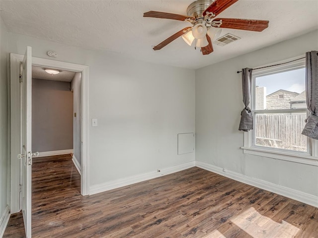 empty room with dark wood-style floors, a ceiling fan, visible vents, and baseboards