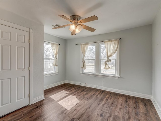 spare room featuring dark wood-style flooring, a ceiling fan, and baseboards