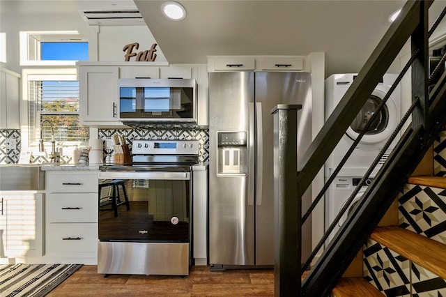 kitchen featuring dark hardwood / wood-style floors, stainless steel appliances, stacked washer and clothes dryer, and white cabinets