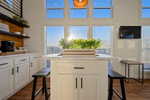 kitchen with a breakfast bar area, white cabinetry, dark hardwood / wood-style floors, a kitchen island, and a high ceiling