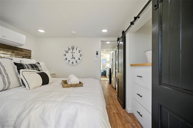 bedroom featuring wood-type flooring, a barn door, and a wall mounted AC